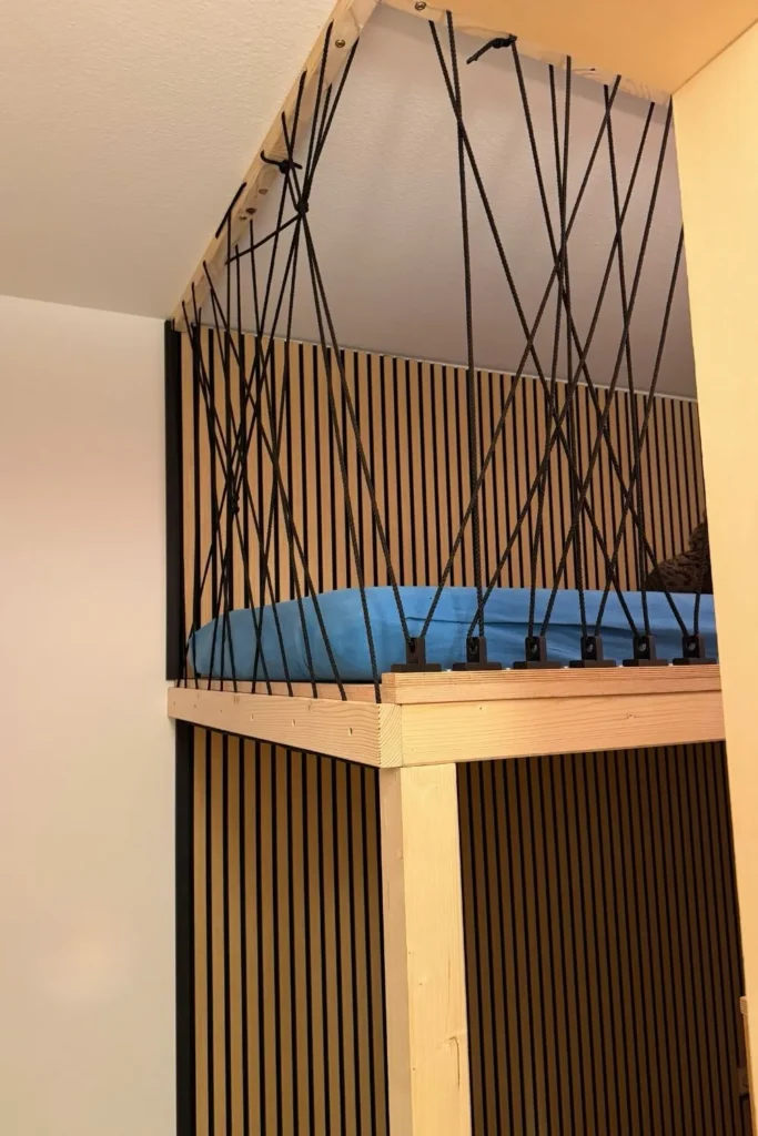 Gesamtansicht eines selbstgebauten Hochbetts mit Holzrahmen, Akustikpaneelen und Seil-Rausfallschutz.