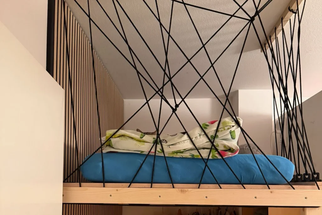 Rausfallschutz aus schwarzen Seilen an einem selbstgebauten Hochbett mit Holzrahmen.