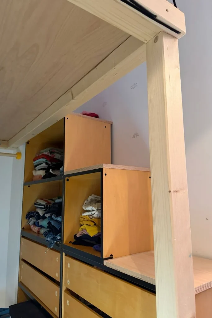 Stauraum unter einem Hochbett mit offenen Schrankkorpussen und Holzpfosten.