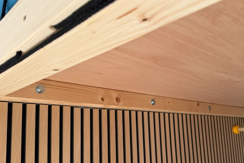 Unterseite der Matratzenebene mit verschraubtem Wandbalken und Akustikpaneelen im Hintergrund.