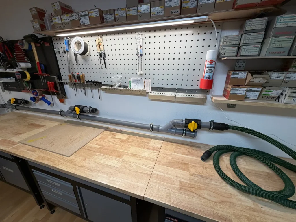Gesamtansicht einer DIY Werkstattabsaugung mit DN50 Rohrsystem oberhalb einer vier Meter langen Werkbank.