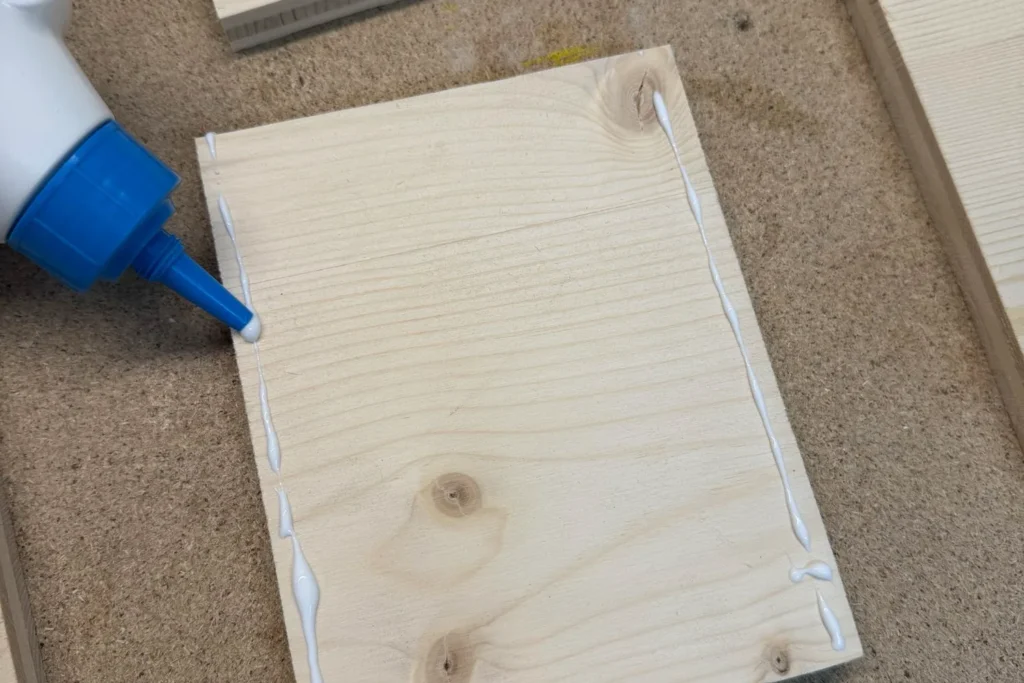 Holzleim wird auf die Kanten der Holzplatten aufgetragen, um den Rahmen der Wildbienen-Nisthilfe zu verleimen