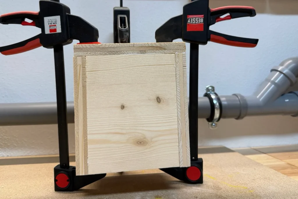 Die verleimte Rückwand der Wildbienen-Nisthilfe wird mit Schraubzwingen fixiert.