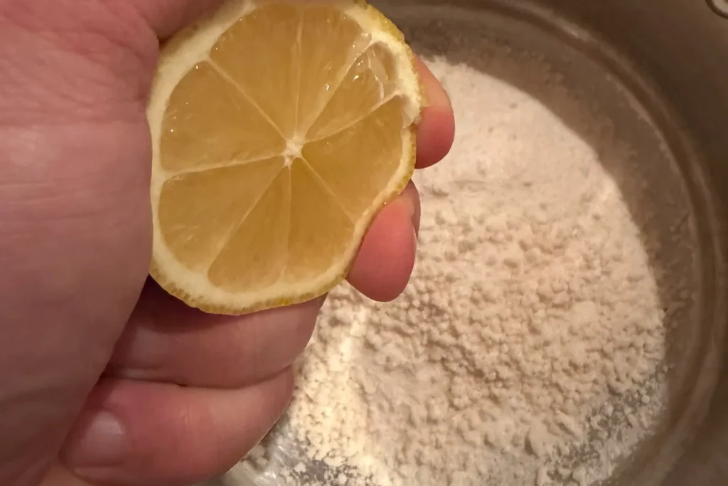 Eine halbe Zitrone wird über Gelierzucker in einem Topf ausgepresst.