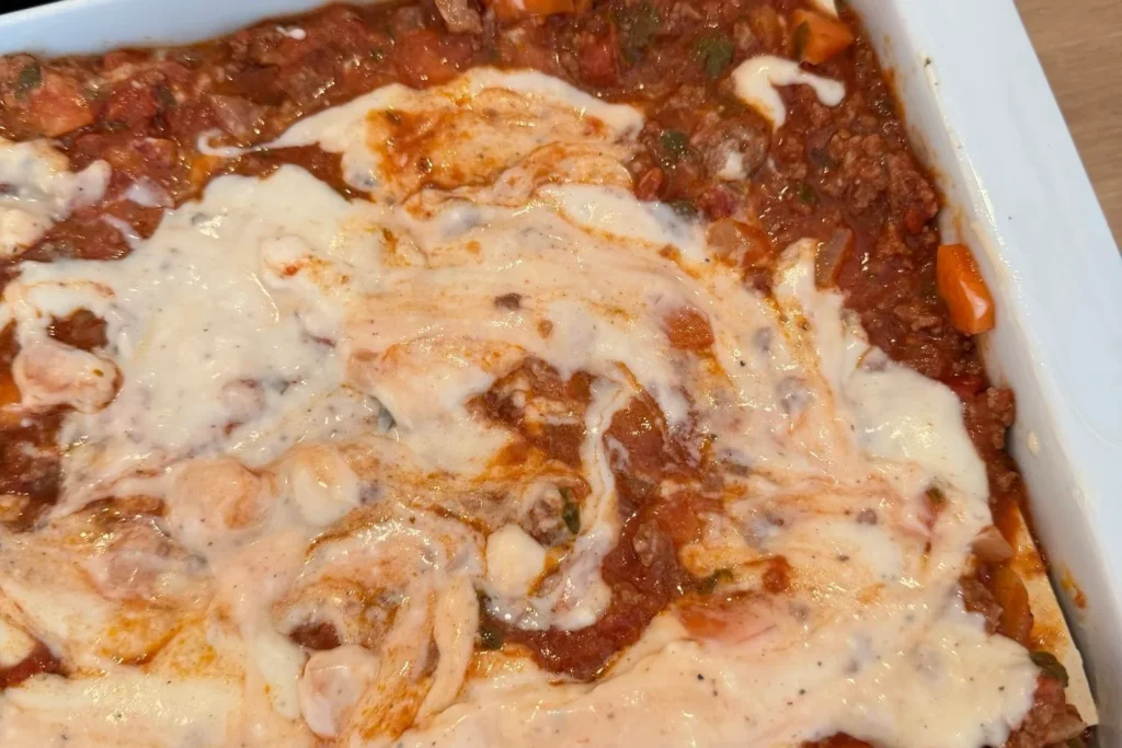 Béchamelsauce wird auf die Rinderhack-Bolognese in der Auflaufform verteilt