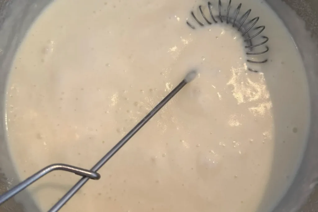 Cremige Béchamelsauce wird im Topf mit Schneebesen glatt gerührt