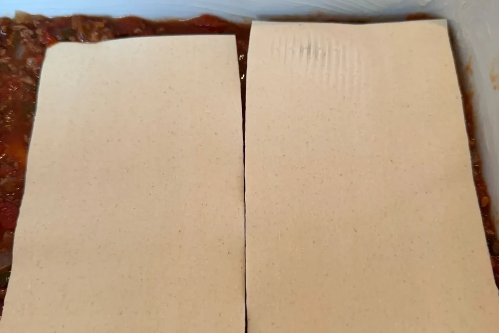 Lasagneplatten werden auf der Rinderhack-Bolognese in der Auflaufform ausgelegt