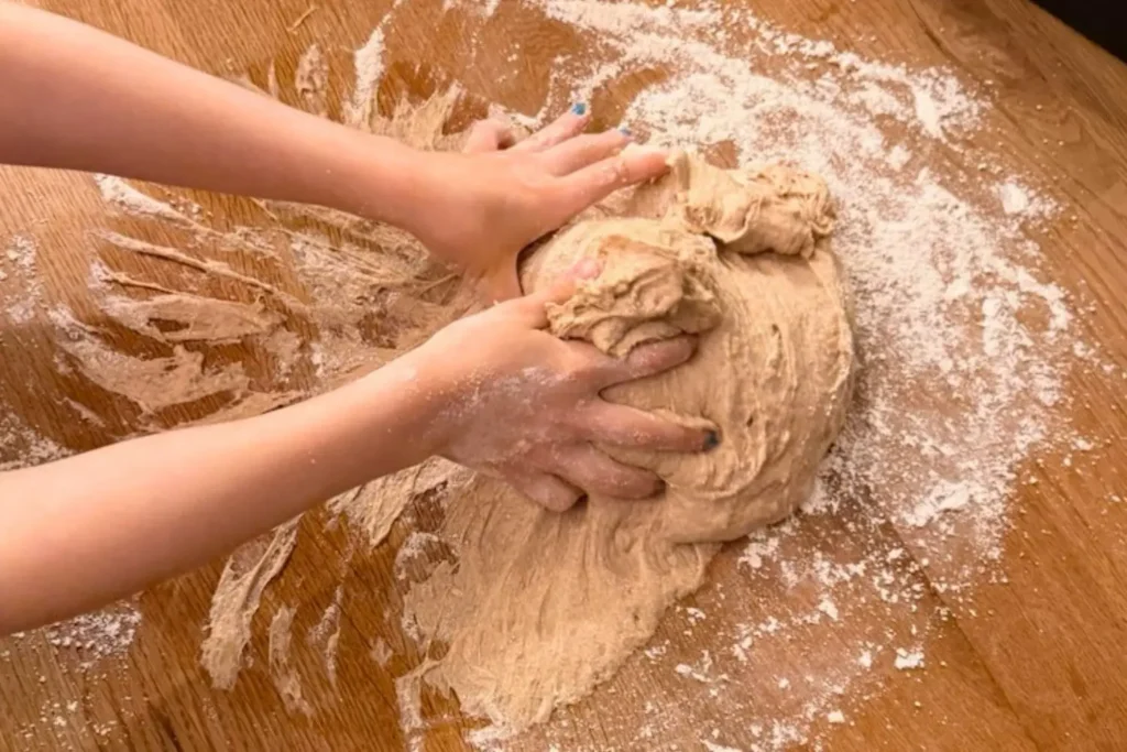 Dinkelvollkorn Teig wird auf einer bemehlten Arbeitsfläche mit den Kinderhänden geformt.