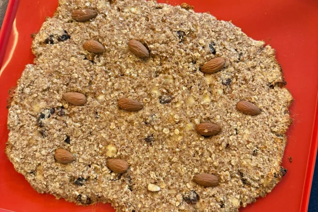 Rohmasse für Müsliriegel aus Trester gleichmäßig auf einer Backform verteilt und mit Mandeln belegt