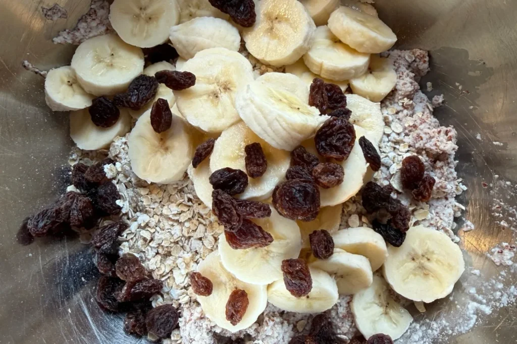 Zutaten für Müsliriegel aus Mandel- oder Haferresten mit Banane, Rosinen und Haferflocken in einer Schüssel