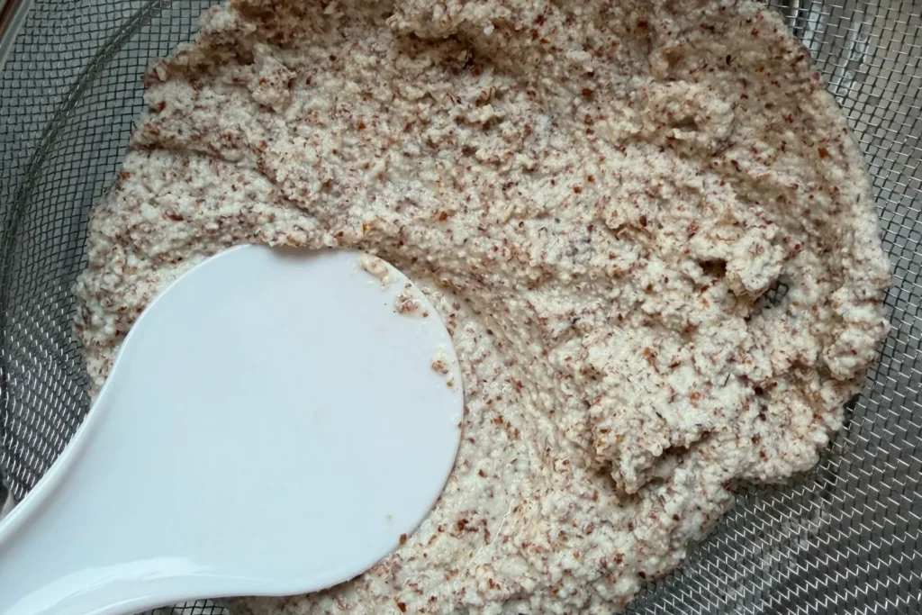 Mandel-Trester wird in einem Sieb ausgedrückt, um überschüssige Flüssigkeit zu entfernen