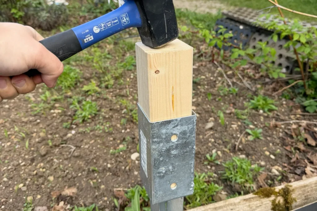 Bodenhülse wird mit Hammer und Holzstück in den Boden geschlagen