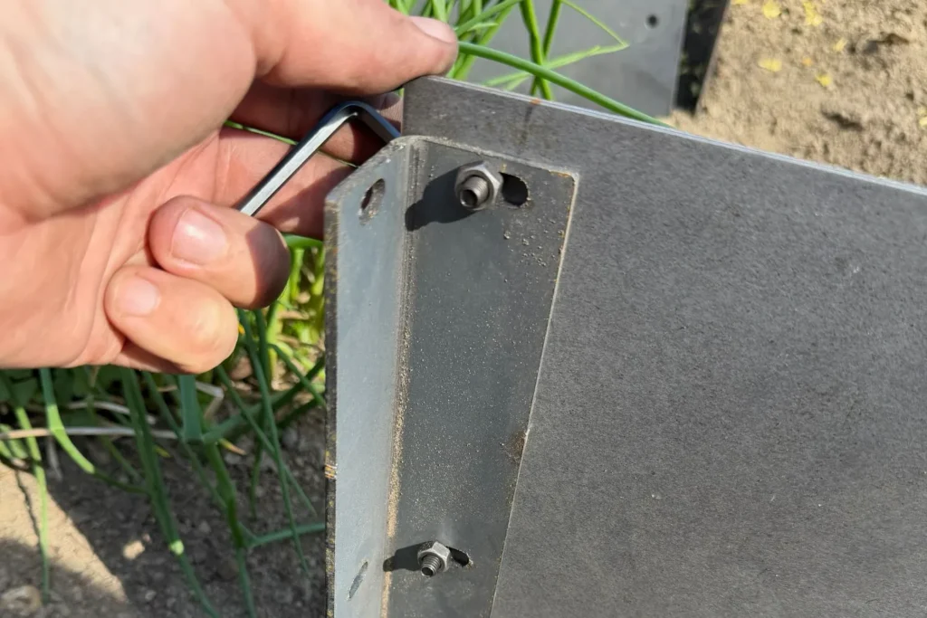 Hand verschraubt Eckverbinder einer Cortenstahl-Beeteinfassung mit Inbusschlüssel