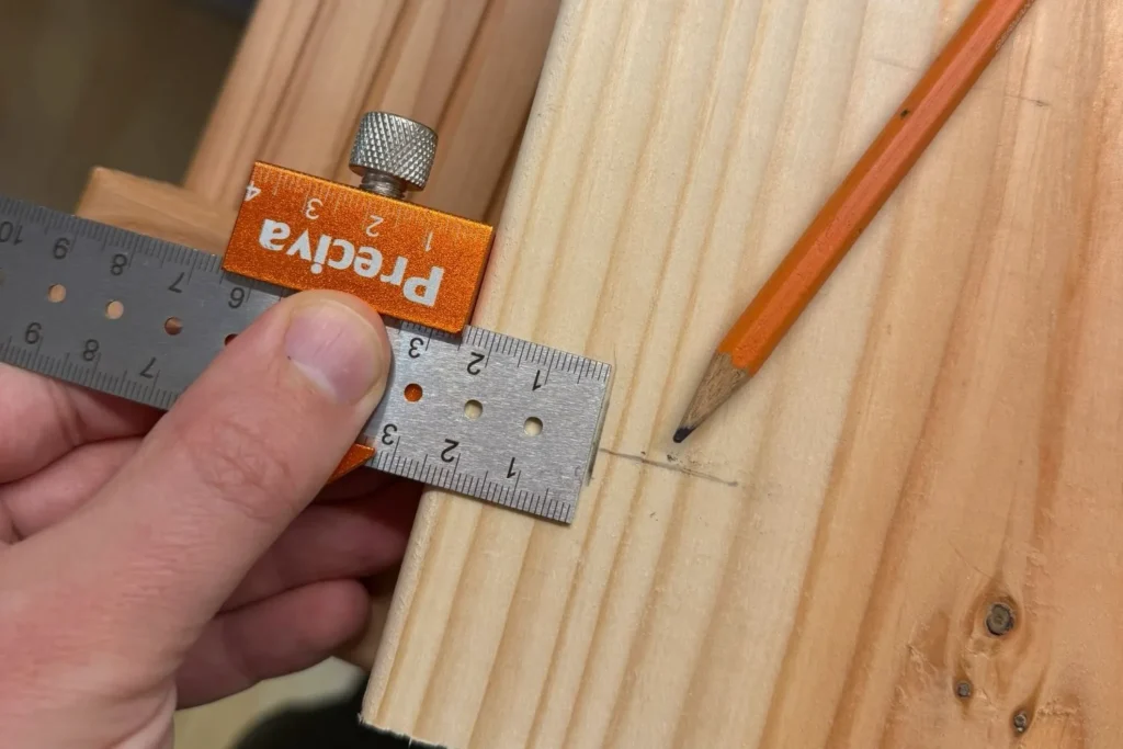 Bohrlöcher auf Holzbrett für Hochbeet werden mit Lineal und Bleistift angezeichnet