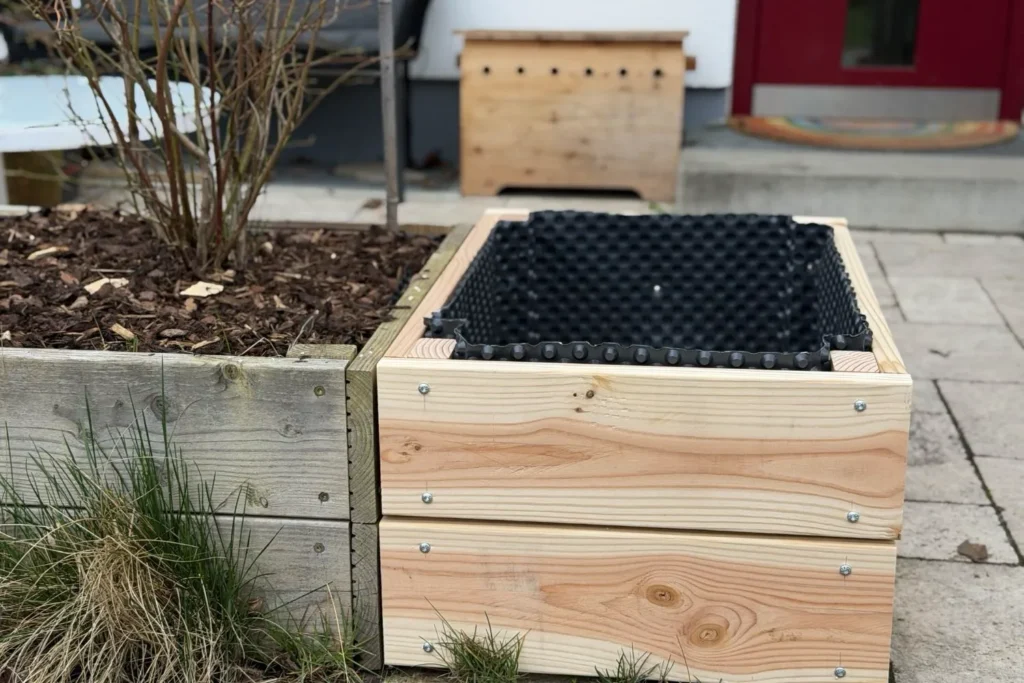 Fertig aufgebautes Hochbeet aus Holz mit Noppenfolie innen vor dem Haus aufgestellt