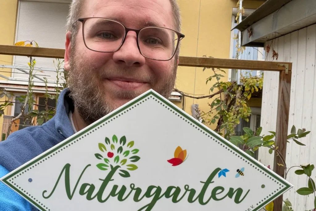 Person hält ein Schild mit der Aufschrift Naturgarten als Auszeichnung für naturnahes Gärtnern