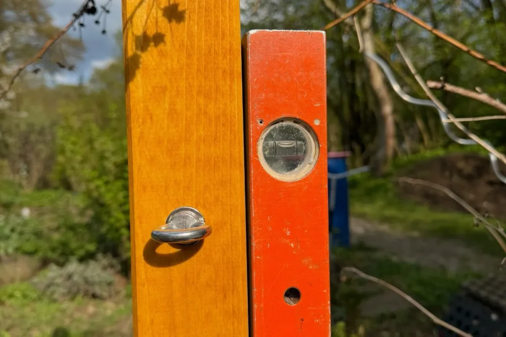 Holzpfosten einer Rankhilfe wird mit Wasserwaage senkrecht ausgerichtet