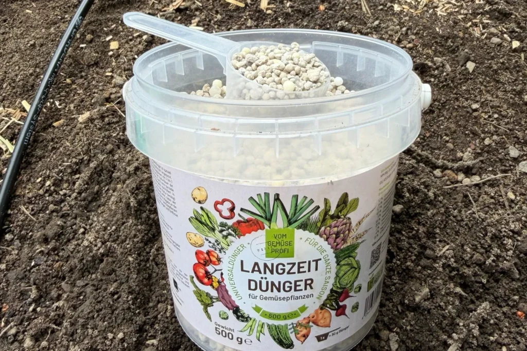 Langzeitdünger für Gemüsepflanzen in einem Beet mit Dosierlöffel