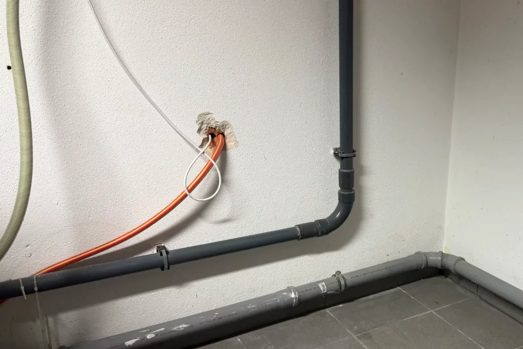 Rohrleitungen und Kabelverlauf an der Wand vor dem Bau des Waschmaschinen-Untergestells.