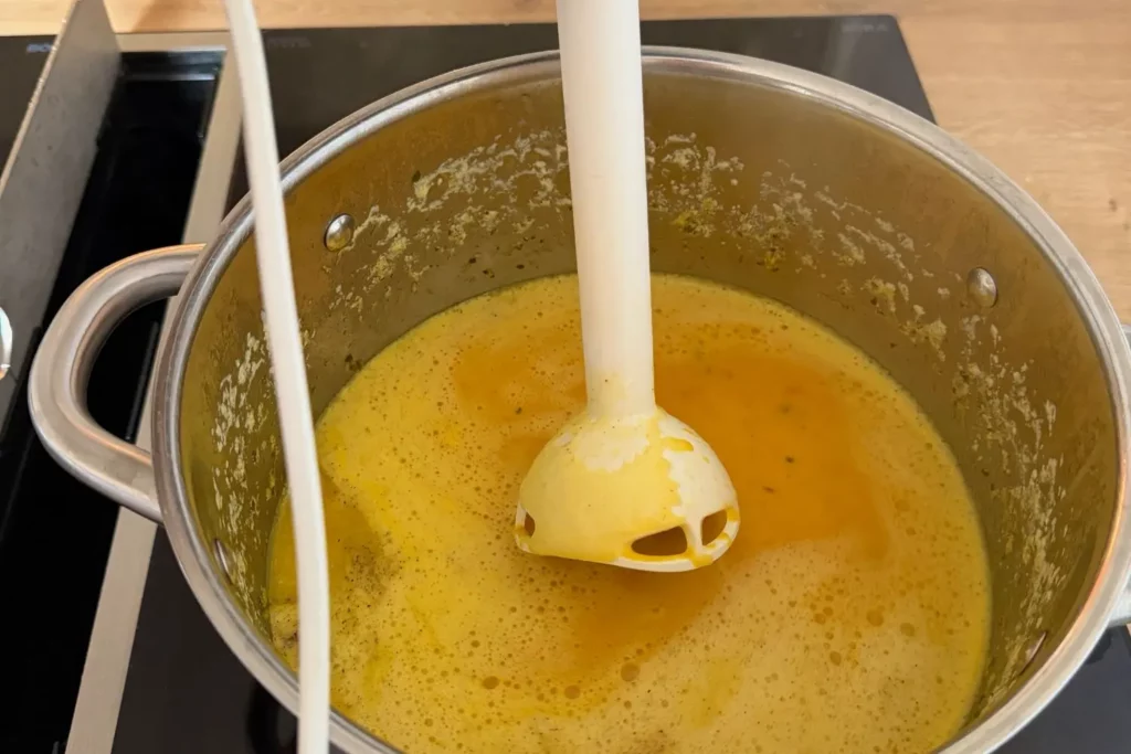 Kürbissuppe mit Kokosmilch wird im Topf mit dem Stabmixer püriert