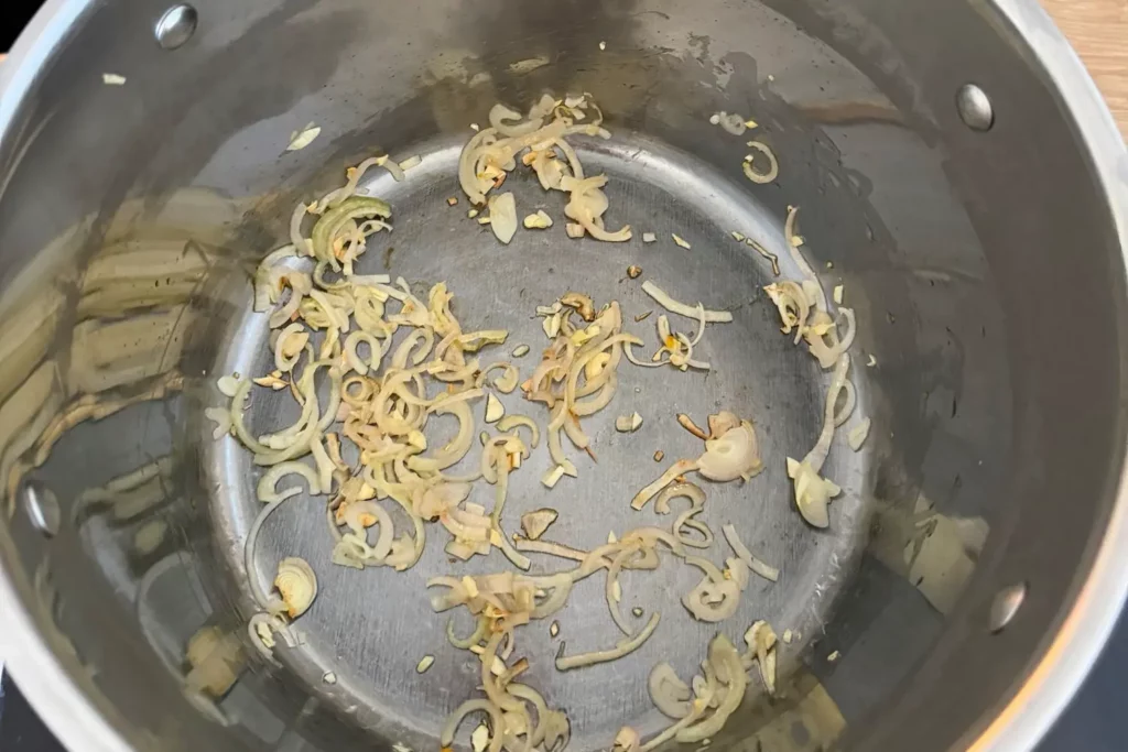 Fein geschnittene Schalotten und Knoblauch dünsten im Kochtopf